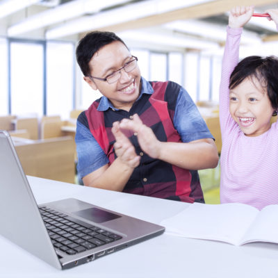 Cheerful student celebrating her success with teacher Portrait of attractive elementary school student celebrating her success in the classroom and her teacher giving applause